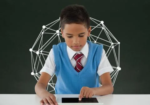 Student boy at table using a tablet against green blackboard with education Stock Photos