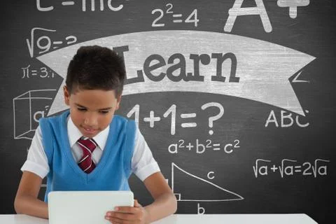 Student boy at table using a tablet against green blackboard with learn text and Fotos Stock