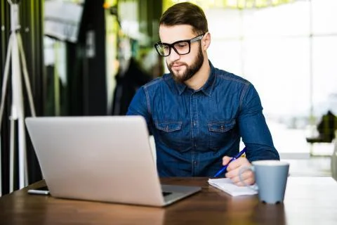 Student busy taking notes down from his new laptop computer while browsing .. Stock Photos