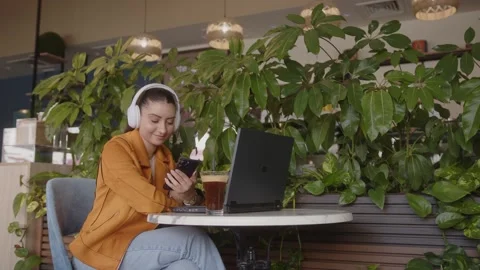 Student checking mobile phone while studying using laptop at cafe Video stock 244601821