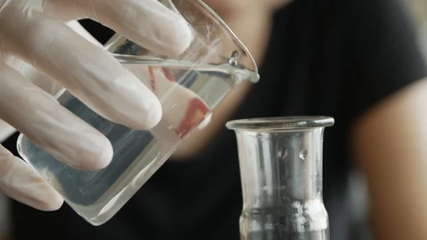 Student chemist pours the reagent from the measuring cup into the flask in ch Stock Footage 113347614