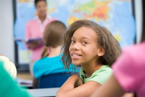 Student in class looking at camera with teacher in background (selective focus) Stock Photos