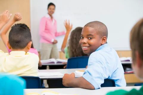Student in class looking at camera with teacher in background (selective focus) Stock Photos