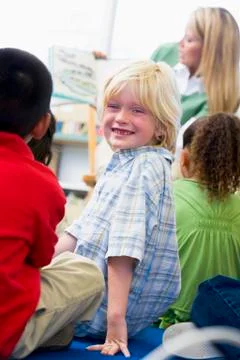 Student in class looking at camera with teacher reading in background (selective Stock Photos