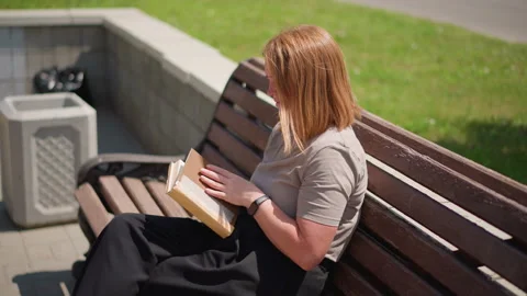 Student Closing Book on Park Bench Under Bright Sunlight Stock Footage 321537343