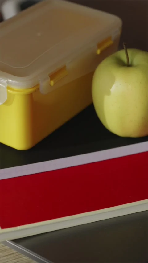 Student desk flat lay with yellow lunchbox green apple and laptop vertical Stock Footage 340139012