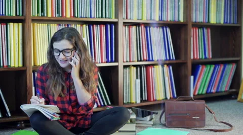 Student doing homework in the library and chatting on cellphone Video stock 59992876