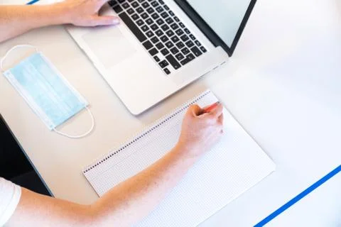 Student doing homework with a notebook and a laptop on a desk with social dis Stock Photos
