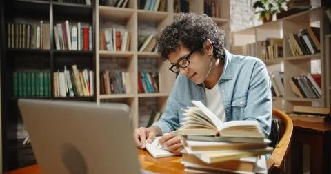 Student is doing research at library using his laptop and books. Nerd is 스톡 사진