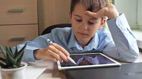 A student draws on a graphic tablet. a boy in a blue shirt is studying at the Stock Footage 168486421