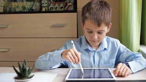 A student draws with a pencil on a tablet. a boy in a blue shirt is sitting at a Stock Footage 169946563