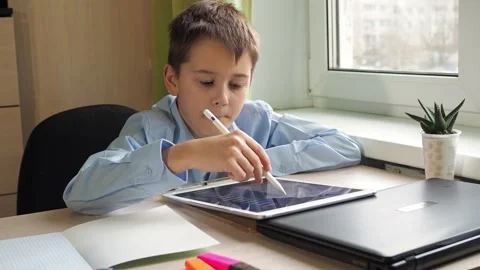 A student draws with a pencil on a tablet. a boy in a blue shirt is sitting at a Stock Footage 172154485