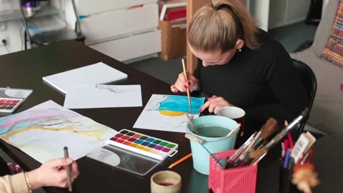 Student draws a picture at table. She brushing paint on paper brush Stock Footage 154826230
