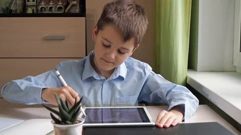 A student draws on a tablet with a pencil. a boy in a blue shirt is studying at Stock Footage 164772585