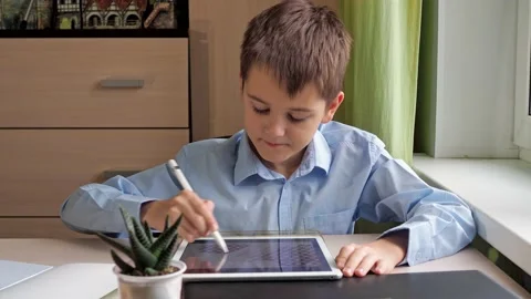 A student draws on a tablet with a pencil. a boy in a blue shirt is sitting at a Stock Footage 171629118