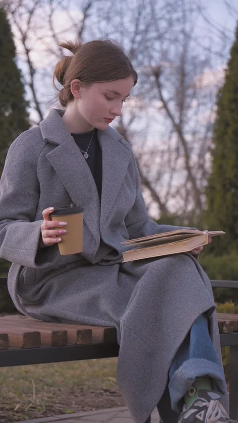 Student drinking coffee and reading a book on a bench Stock Footage 309782224