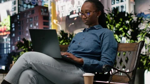 Student drinking coffee on park bench, using laptop to do homework Video stock 334171967