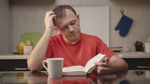 Student drinks tea and reads a textbook sitting in the kitchen, self-education Stock Footage 130912383