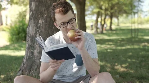 Student eating apple and reading book in the park, steadycam shot Vídeos de archivo 78634031