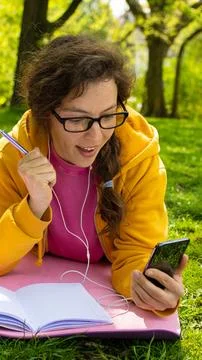 A Student Engaged with Their Phone While Relaxing in a Sunlit Park on a Stock Photos