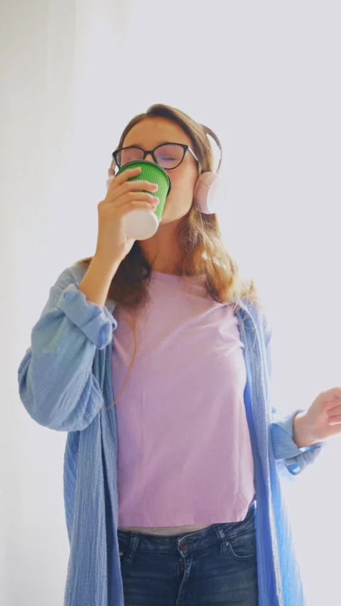 Student enjoying coffee while dancing with headphones on white background. Great Stock Footage 312640356