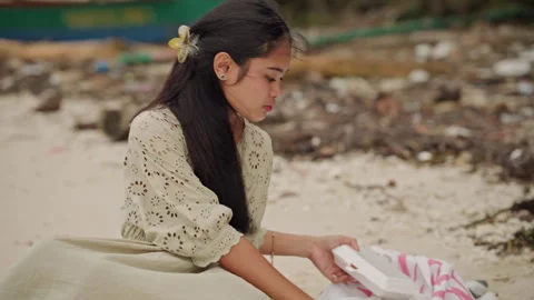 Student examines package beside shoreline. Asian woman pauses to read letter Stock Footage 341664010
