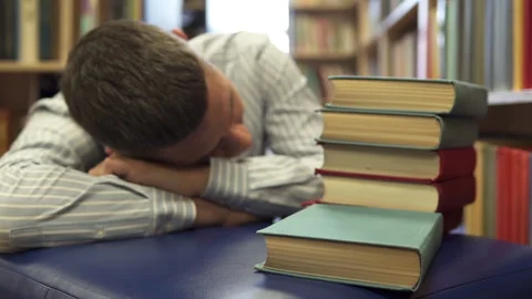 The student fell asleep between the rows of bookshelves preparing for the exam. Stock Footage 219675758