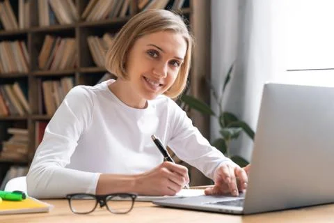 Student girl is looking in a camera while studying in a library using a laptop. Stock Photos