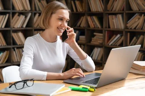 A student girl is studying in a library using a smartphone and a laptop. Stock Photos
