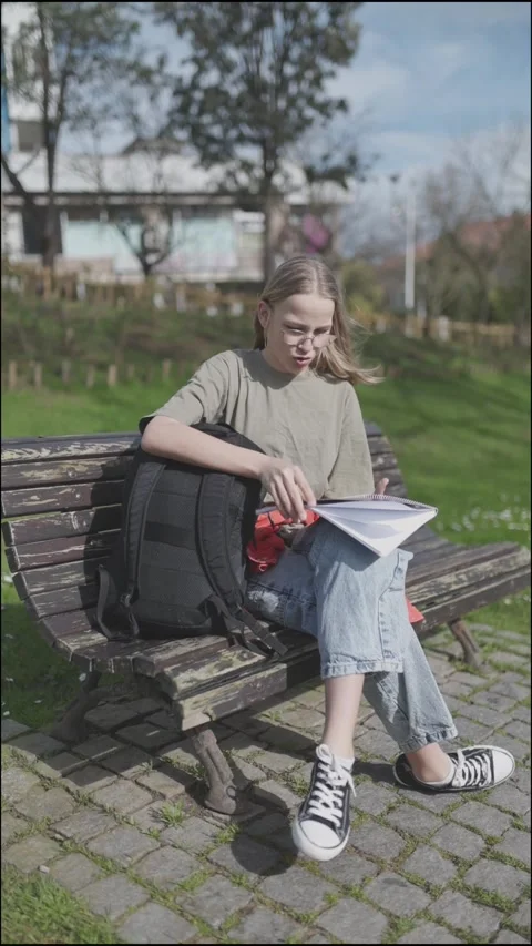 Student girl taking book from backpack and reading on bench in park Stock Footage 314066005