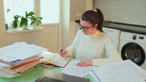 A student with glasses in e-learning, surrounded by documents while working on a Stock Footage 274103393