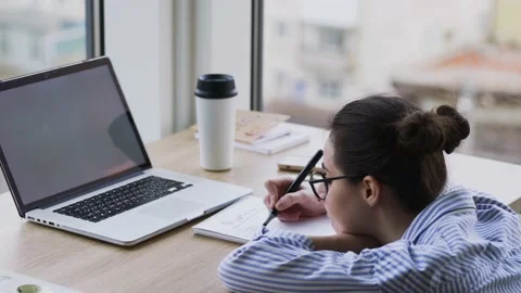 Student with glasses writes in copybook looking in laptop Stock Footage 152533837