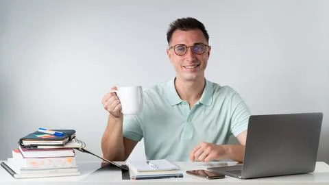 A student guy drinks coffee at a table with textbooks, books, a laptop Stock Photos