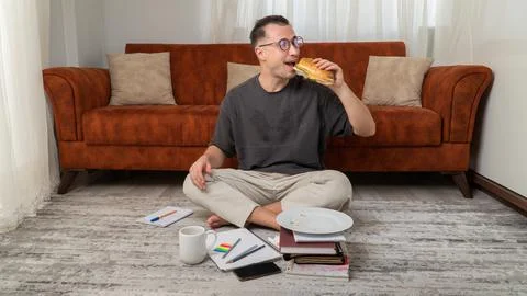 A student guy eats a sandwich while studying at home Stock-Fotos