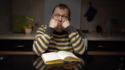 Student guy sitting thinking over a textbook while sitting at the kitchen Stock Footage 130955520