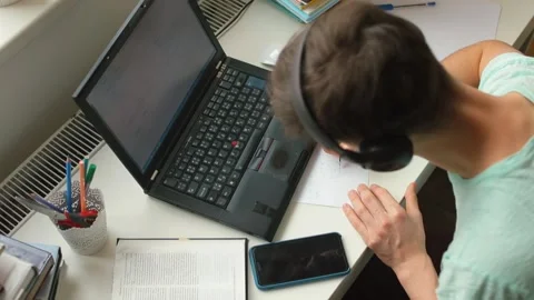 Student guy uses laptop study home, he listens to words, makes notes on paper. Video stock 153242667