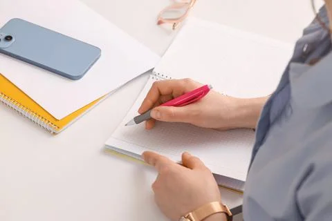 Student hand writing notes in grid notebook with pen, smartphone, and glasses Stock Photos