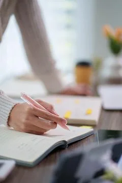 Student hand writing notes in notebook with pen during study session at bri.. Stock Photos