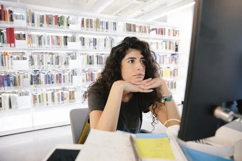 Student with hands on chin using computer in university library Stock Photos