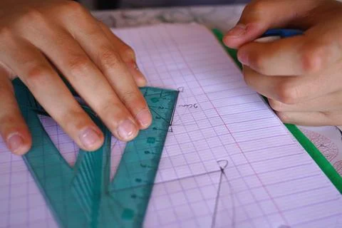 Student hands using a green triangle ruler to draw geometric shapes in a ma.. Stock Photos
