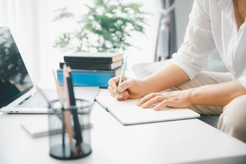 Student hands writing notes in notebook beside laptop and books on desk in .. 库存照片