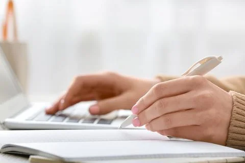 Student hands writing notes in notebook while typing on laptop keyboard for o Stock Photos