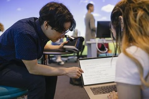 Student helping friend with computer code on laptop in VR class Stock Photos