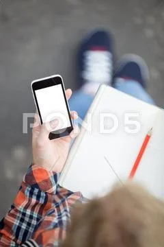 Student holding a smartphone against an open copybook Stock Photos