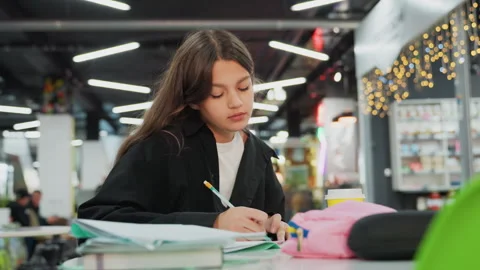 Student intently taking notes at welllit public area in shopping center 스톡 동영상 329889519
