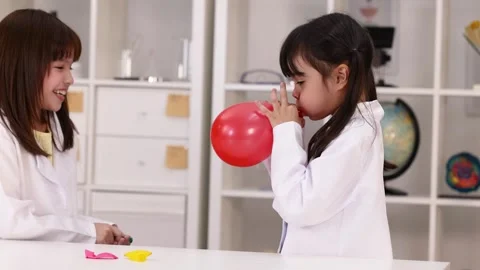 Student in Lab Coat Blowing Up Red Balloon for Science Experiment Stock Footage 344943986