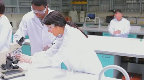 Student in lab coat  looking through a microscope Stock Footage 12779133