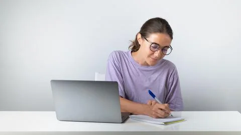 A student at a laptop makes notes in a notebook, studies Stock Photos