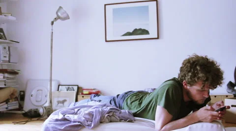 A student is laying in bed, while he is using a smartphone. Stock Footage 40358074