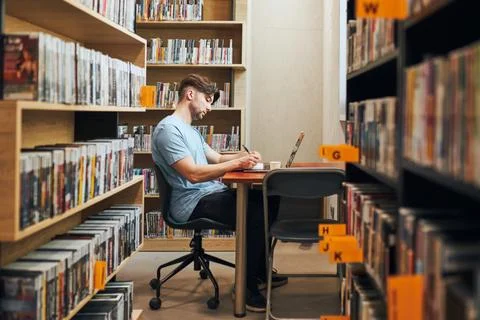 Student learning in library. Young man preparing for test on laptop. Man li.. Stock Photos